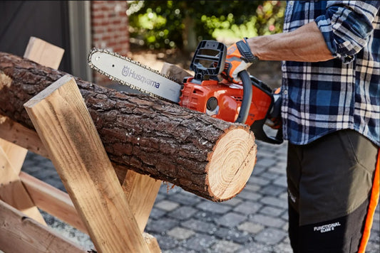Person using a husqvarna chainsaw to cut a log with a blurred background