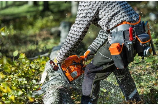 Person using a husqvarna chainsaw to cut a log with a tool belt in the foreground