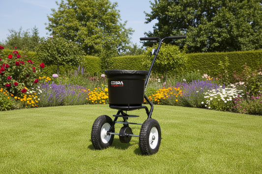 A black Cobra broadcast spreader with a large hopper, three wheels, and a handle.