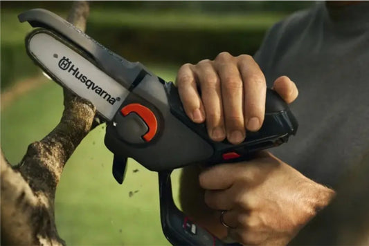 Person holding a Husqvarna chain saw with a blurred natural background