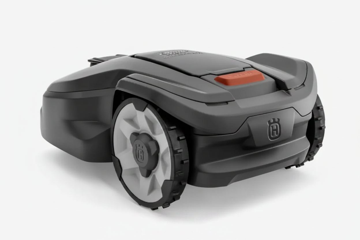 A Husqvarna robotic lawnmower shown from a three-quarters angle on a light gray background. The mower is primarily dark gray with a small orange accent on top and a Husqvarna logo on the front bumper.