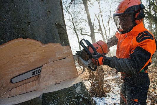 Person in stihl orange safety vest using a chainsaw to cut a tree trunk outdoors.